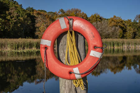 Orange Lifesaver Strapped to Wooden Post next to calm lakeの写真素材