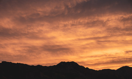 Pink and Yellow Light Brightens Wafting Clouds Over Silhouettesの写真素材