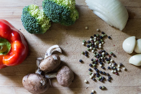 Healthy Eating Vegetables on Wooden Cutting Board, Peppercorns, Red Bell Pepper, Onion, Garlic, Broccoli, Mushroomの写真素材
