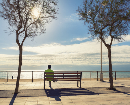 man tourist resting  on a bench and looking at the beachの写真素材