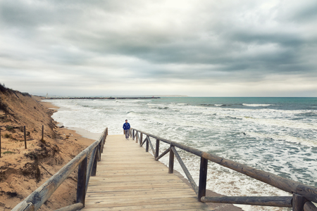 Man walking on boardwalk  in a stormy and clouded day in the Mediterranean sea. Guardamar del segura, alicante. Spainの写真素材