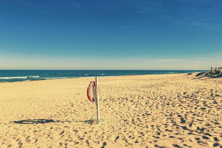 life buoy hanging on a pole in sandy beach and footprints