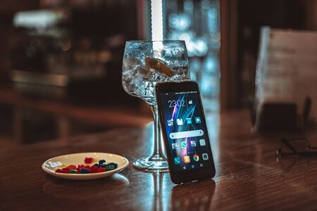 smartphone put on a refreshing glass of gin tonic in a bar at nightの写真素材