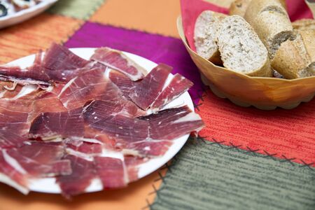 view of a white plate with messy slices of ham and appetizers with black olives