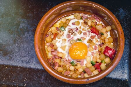 baked egg on squares of fried potatoes and pieces of bacon with peppersの写真素材