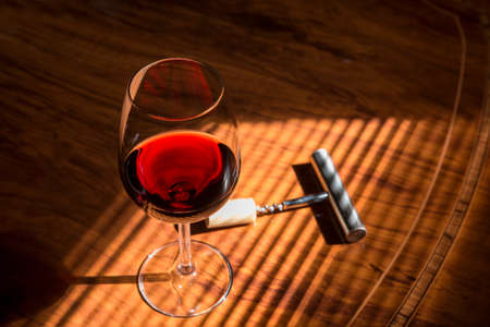 close-up of red wine glass on table with corkscrew with shades of a blind