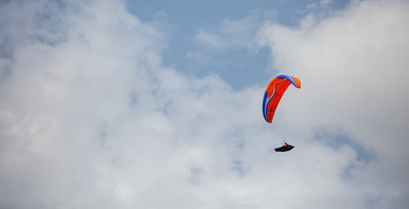 Paraglider flying in the blue sky with white clouds.