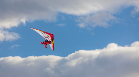Hang glider flying in the blue sky with white clouds.