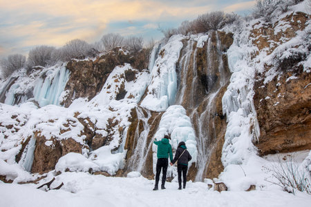 Couple standing in front of the waterfall in winter. Winter landscape