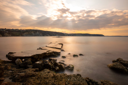 Sunset over the sea with rocks and jetty on the shore