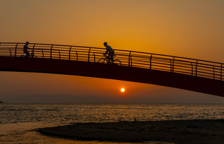 Silhouette of a cyclist on the bridge over the sea at sunsetの写真素材