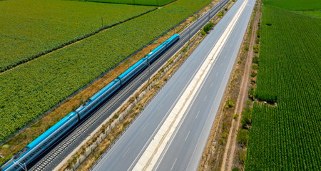 Aerial view of the highway with blue train passing through green field