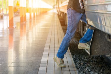 Young tourist man feet step up to a passing train at the train station.の写真素材