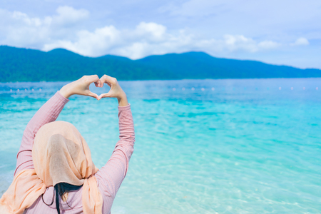 Beautiful of happy young woman  lift hand showing heart shape at lipe thailand island with the turquoise ocean water.の写真素材