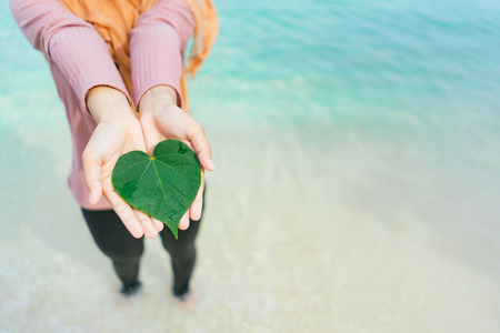 woman's hands holding a heart shape of Green Leaves
 at lipe thailand island with the turquoise ocean water and white sand.Ecology concept, World Environment Day, Earth Day.Hope, New Life or csr activities.の写真素材
