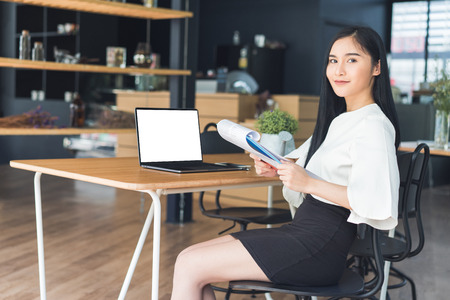 Young business woman reading a report sitting in a coffee shop and working on blank screen laptop.の写真素材