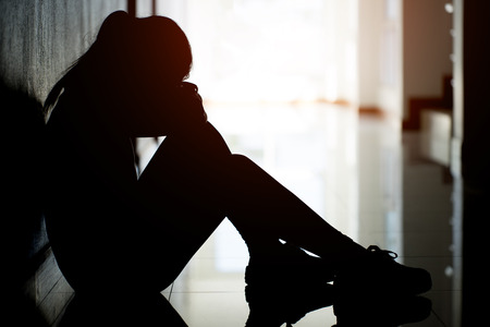 Silhouette of sad and depressed women sitting at walkway of condominium or office with backlit,sad mood,feel tired, lonely and unhappy.の写真素材