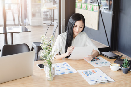 Asian beautiful young business woman in white shirt smiling working on desk with laptop and financial report document.の写真素材