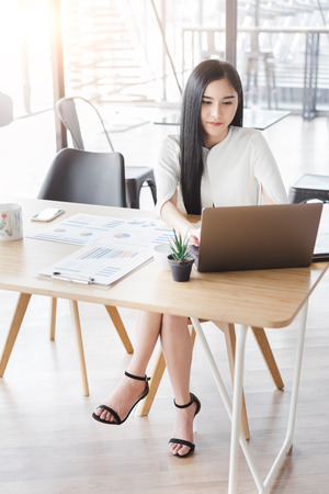 Asian beautiful young business woman in white shirt smiling working on desk with laptop and financial report document.の写真素材