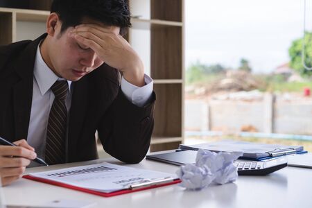 Depressed young male accountant working with report document and calculator. Negative human emotion facial expression feelings.の写真素材