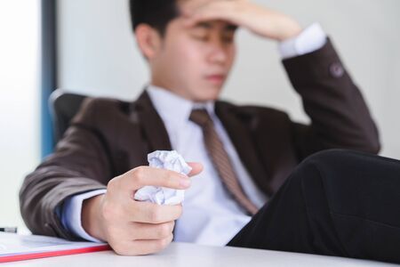 Unhappy young businessman hand holding a crumpled paper and another squeezing head with hand. Negative human emotion facial expression feelings.の写真素材