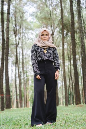 Portrait of happy young muslim woman mellow yellow hijab over blurred the pine forest background. Vintage tone.の写真素材