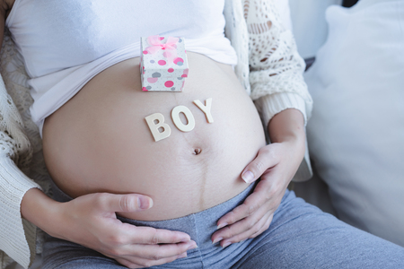 Young beautiful pregnant woman sitting on sofa and BOY alphabet on her belly.a boy conceptの写真素材