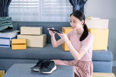 Attractive asian teenage start up running small business owner take a photo of products with smartphone from home office.の写真素材
