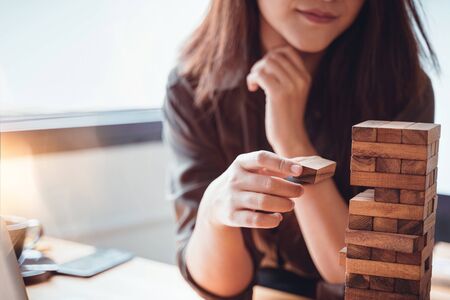 Young female hand placing or pulling wooden block on the tower balance game. Business planning, Risk...
