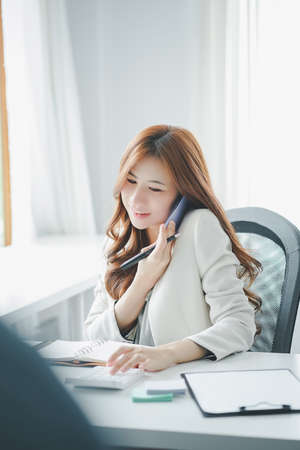 Female accountant using calculator and talking on telephone while sitting in an office.の写真素材