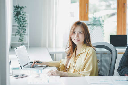 Female accountant using calculator and talking on telephone while sitting in an office.の写真素材