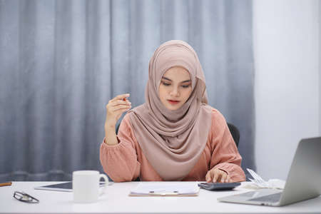 Stressed muslim woman calculating monthly financial, plan budget on computer, pay bills or taxes online at home.の写真素材