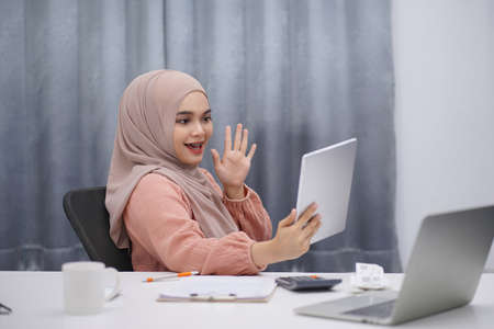 Beautiful asian muslim woman brown hijab having video call with friends or lover, using digital tablet at her home.の写真素材