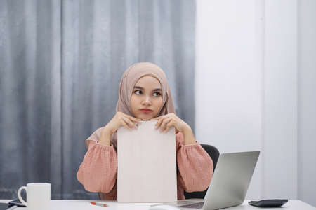Tired asian muslim woman brown hijab working at home with laptop and documents.の写真素材