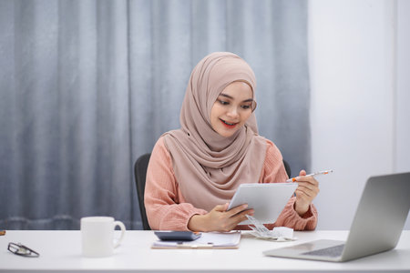 Beautiful asian muslim woman brown hijab having video call with friends or lover, using digital tablet at her home.の写真素材