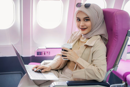 Beautiful asian muslim business woman working on digital laptop computer and drinking coffee during the flight.の写真素材