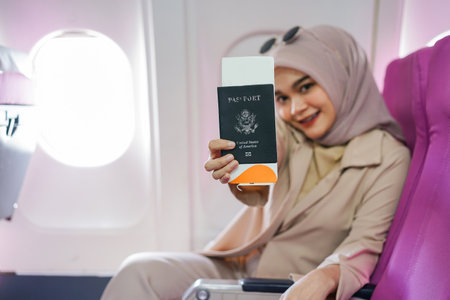 Beautiful asian muslim female traveler passengers showing us passport and air ticket in an airplane.の写真素材