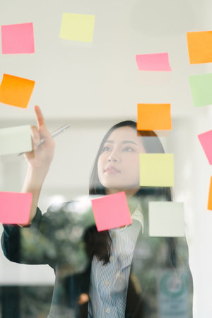The concept of brainstorming is exemplified as a businesswoman shares ideas using Postit notes,...