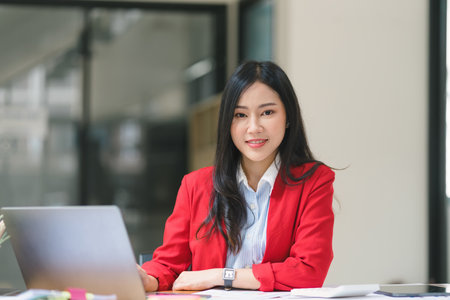 An attractive young businesswoman is using a laptop in a modern office and looking at the camera.の写真素材