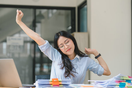 An attractive young businesswoman is stretching her arms during a break at the office.の写真素材