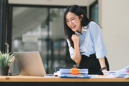 A businesswoman celebrates with her arms up while looking a laptop in a happy and successful pose.の写真素材