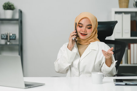 An attractive young Muslim businesswoman is talking on her smartphone in a modern office.の写真素材