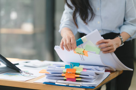 A businesswoman is seen at her desk, searching and checking through stacks of paper files and folders containing unfinished documents and achieved papers.の写真素材