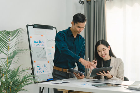 Startup young Asian-Caucasian colleagues are discussing work together on a tablet, with a male worker engaging in conversation with his female coworker. This depicts the concept of collaboration.の写真素材