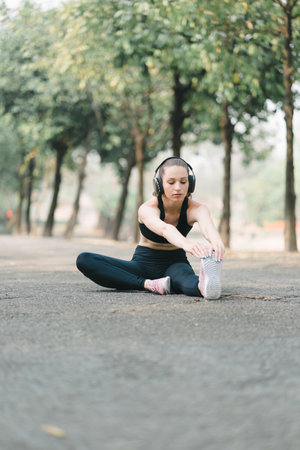A beautiful sportswoman in sportswear is stretching her body with a smile on her face, while doing...