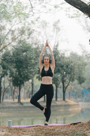 A beautiful and attractive Asian woman is practicing the Lotus pose in an Autumn city park background.の写真素材