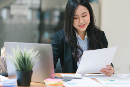 A beautiful Asian businesswoman is using a digital laptop at her desk in a modern office.の写真素材