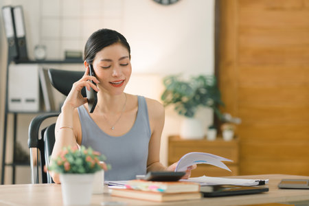 A beautiful young businesswoman is shown working on a laptop computer in her home office. The image represents the concept of working from home.の写真素材