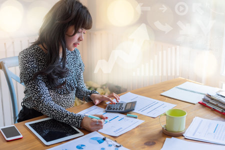 Happy beautiful asian accountant woman sitting at her work place in a light modern design office and using calculator.financial or accounting concept.の写真素材
