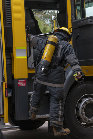 A behind view of a firemen climbing down from a yellow fire engine with there full uniform and oxygen tank onの写真素材